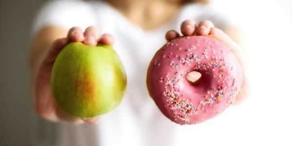 person holding an apple and a donut to choose from